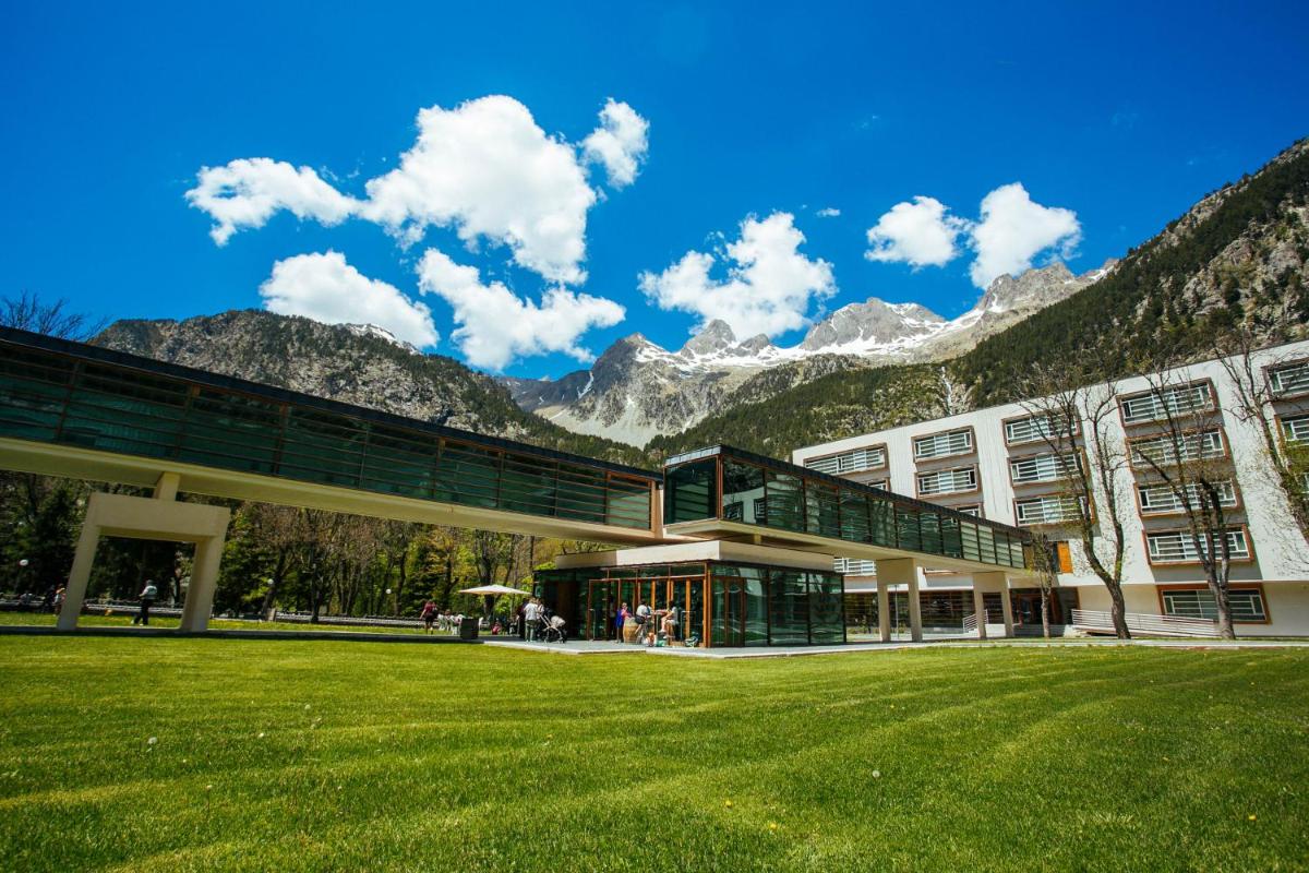 Un edificio con un campo de hierba frente a una montaña. en Hotel Continental Balneario de Panticosa, en Panticosa