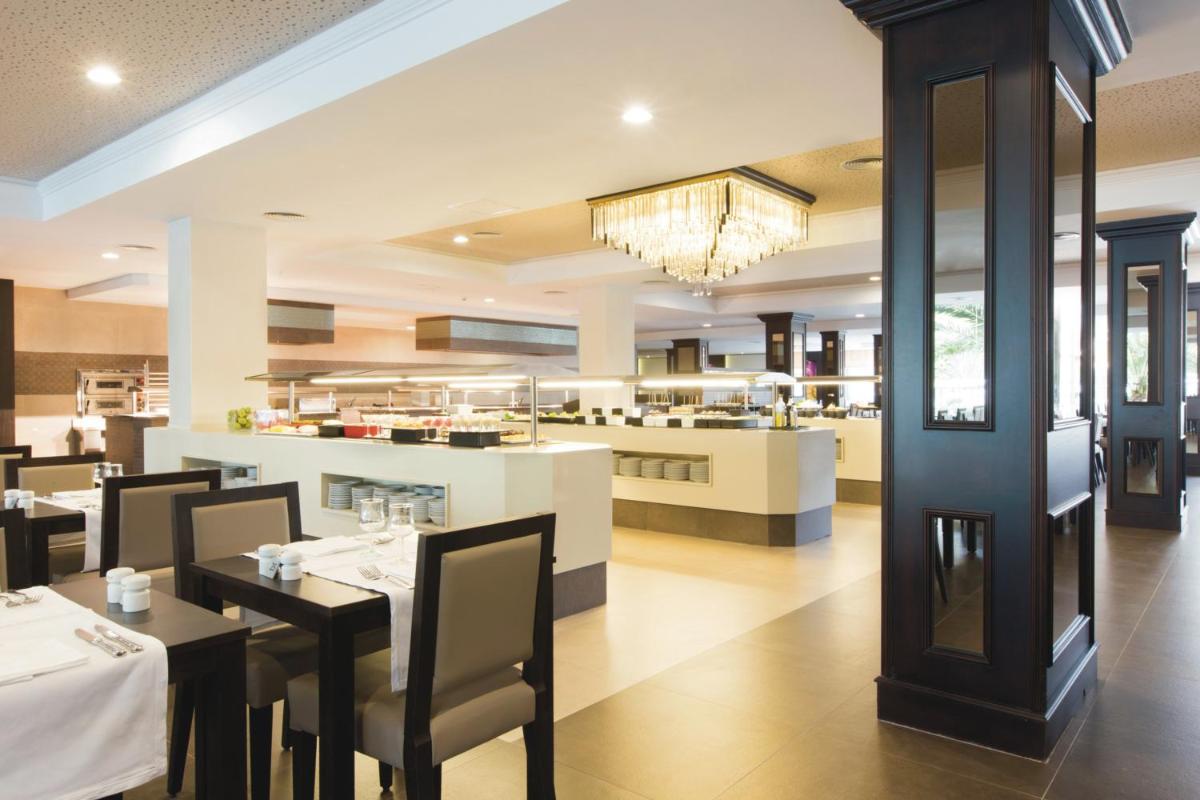 Un comedor con mesas y sillas y un restaurante. en Hotel Riu Bravo - 0'0 All Inclusive, en Playa de Palma