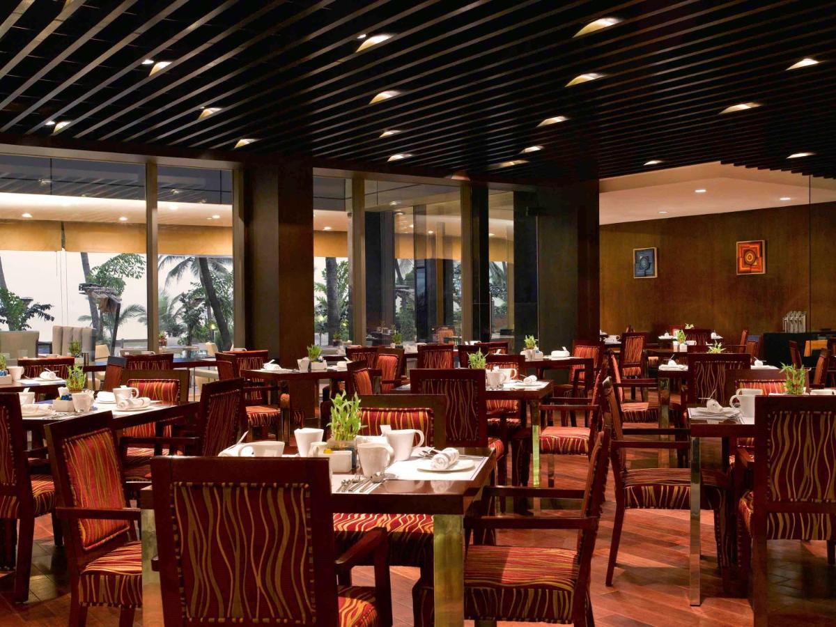 a dining room with tables and chairs and windows at Novotel Mumbai Juhu Beach in Mumbai
