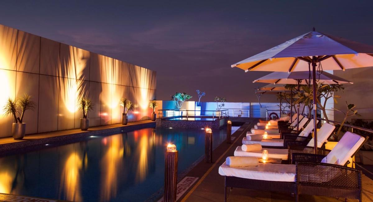 a pool with chairs and umbrellas next to a building at Radisson Blu Hotel Pune Kharadi in Pune