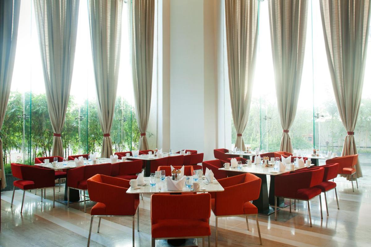 a dining room with tables and red chairs and windows at Radisson Blu Hotel Pune Kharadi in Pune