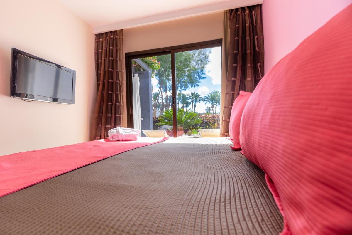 1 dormitorio con 1 cama grande de color rojo y TV de pantalla plana en R2 Romantic Fantasia Suites - Adults Only, en Tarajalejo
