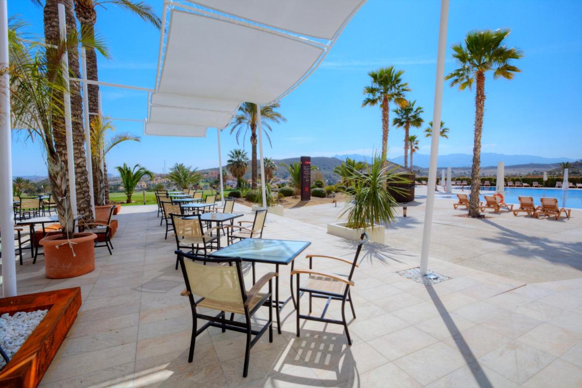 Un patio con mesas y sillas y palmeras. en Hotel Valle del Este, en Vera