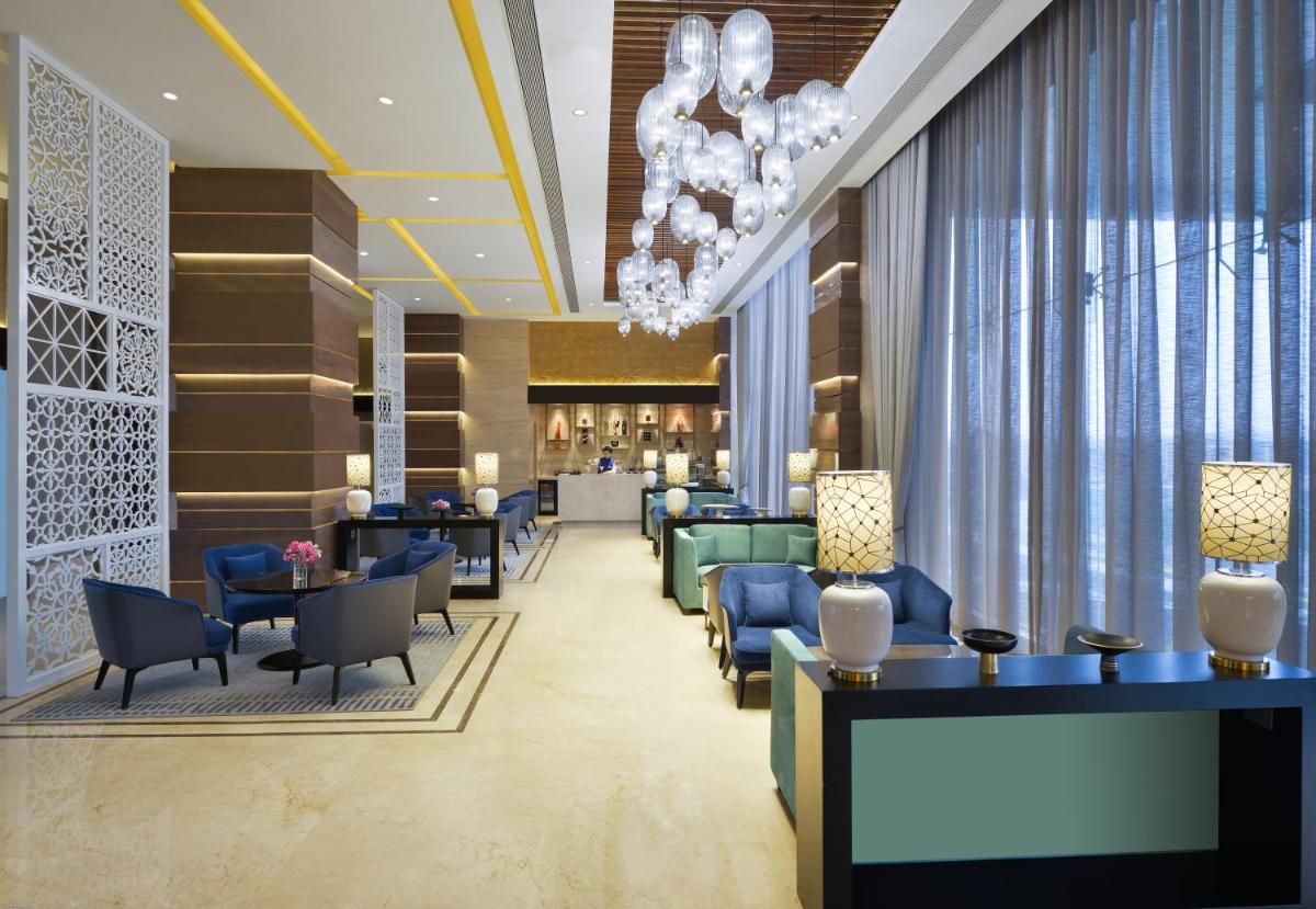 a lobby with blue chairs and tables and a chandelier at Taj Skyline Ahmedabad in Ahmedabad