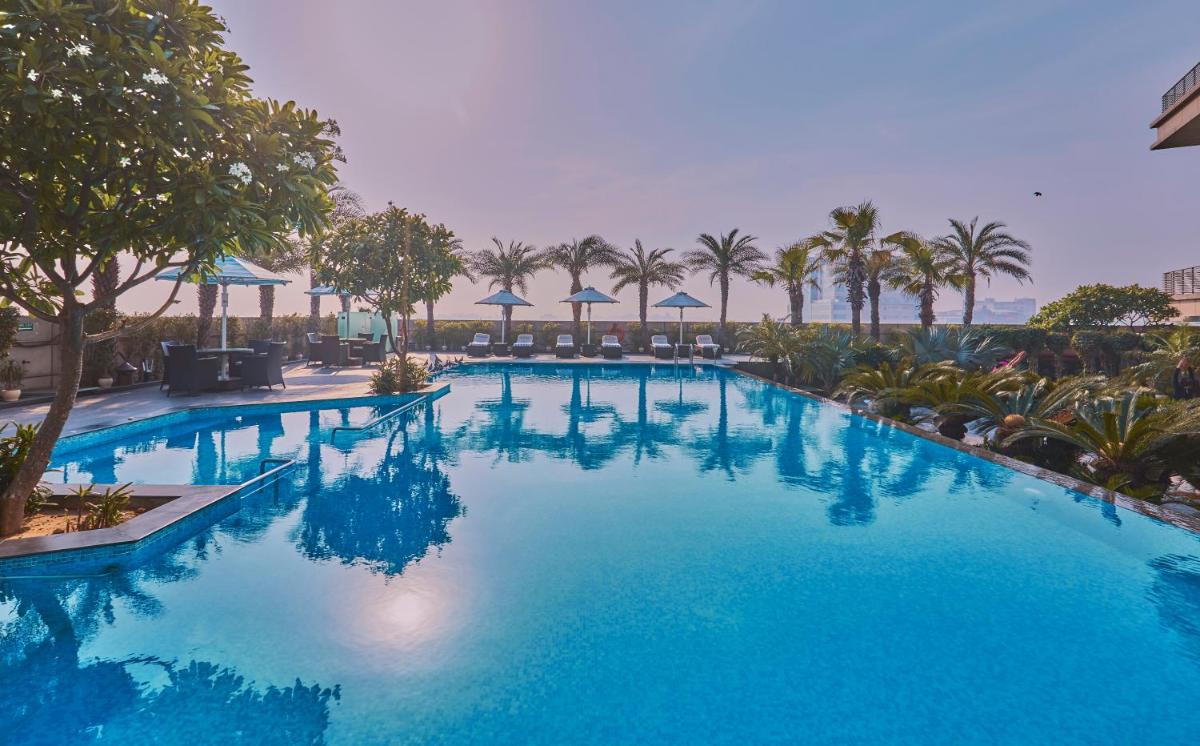 a large blue swimming pool with palm trees and umbrellas at Crowne Plaza New Delhi Rohini by IHG in New Delhi a large blue swimming pool with palm trees and umbrellas at Crowne Plaza New Delhi Rohini by IHG in New Delhi
