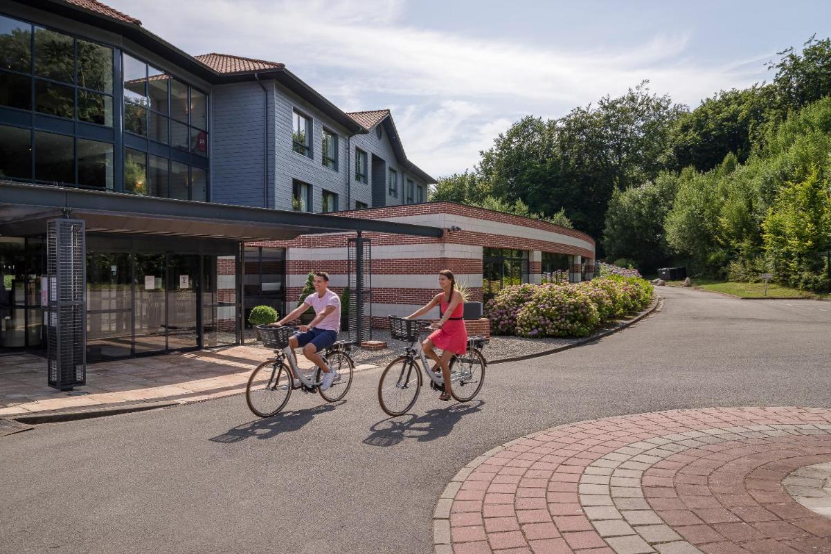 deux femmes faisant du vélo dans une rue devant un immeuble dans l'établissement Hôtel du Golf, à Lumbres