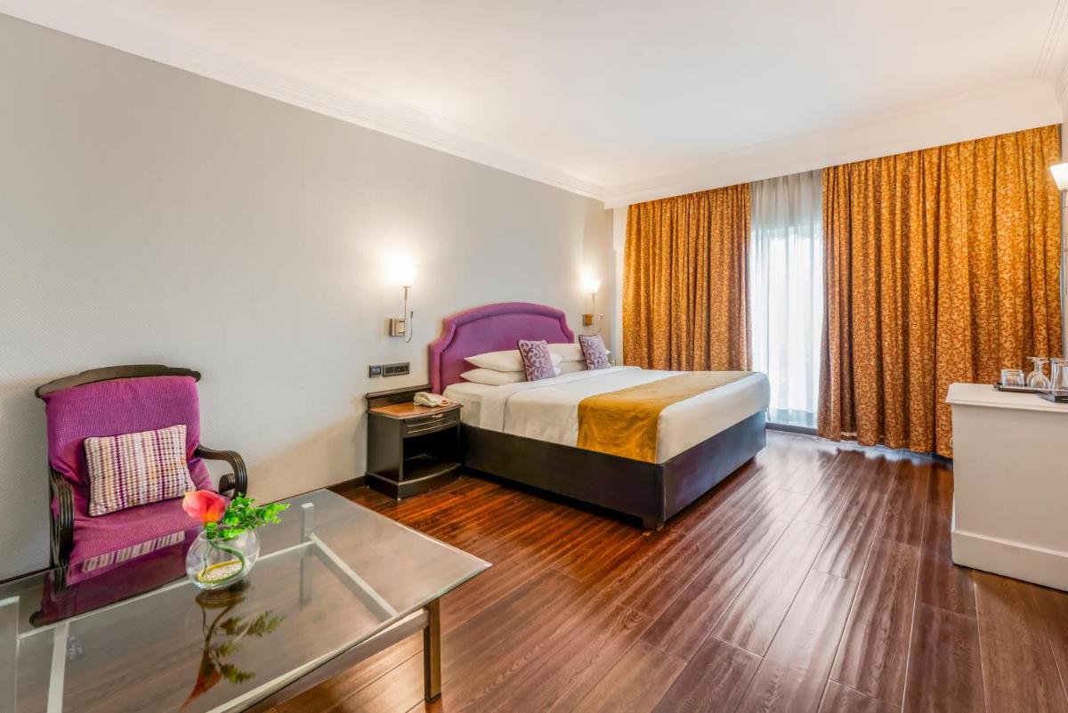 a hotel room with a bed and a couch and a table at Hotel Royal Orchid Bangalore in Bengaluru