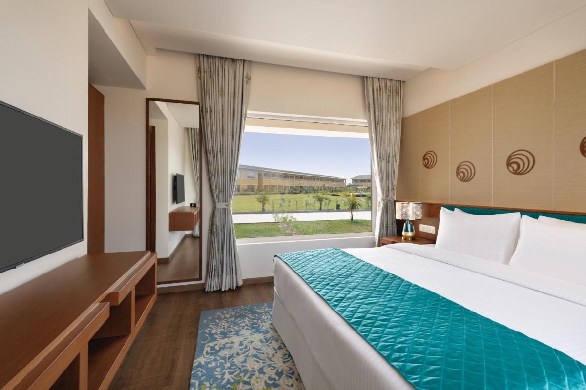 a hotel room with a bed and a large window at Hawthorn Suites by Wyndham Dwarka in Dwarka a hotel room with a bed and a large window at Hawthorn Suites by Wyndham Dwarka in Dwarka