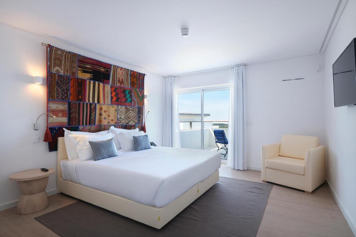 um quarto branco com uma cama branca e uma cadeira em Royal Obidos Scenic Resort em Praia del Rei
