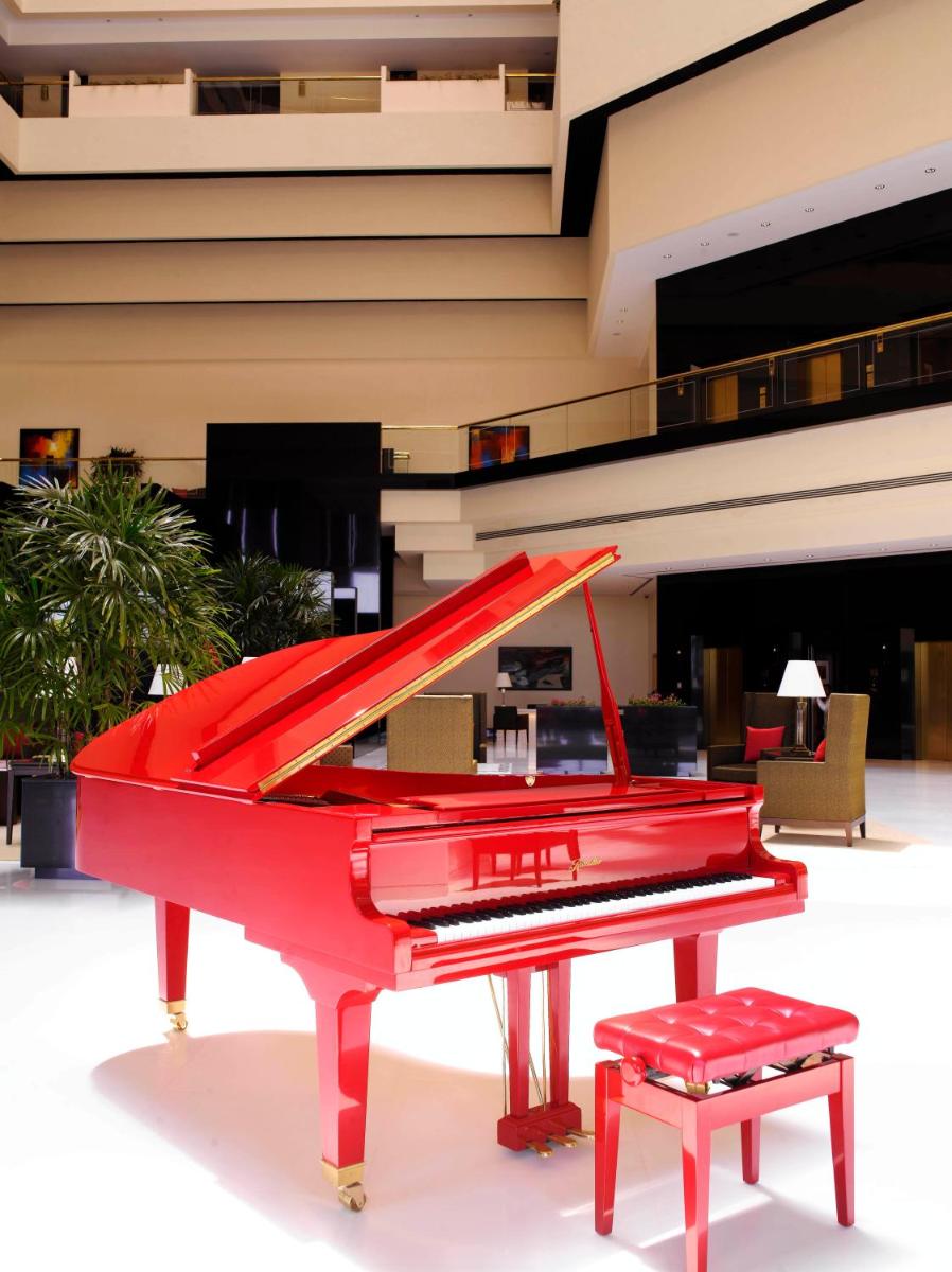 a red piano with a stool in front of a building at The Oberoi Mumbai in Mumbai