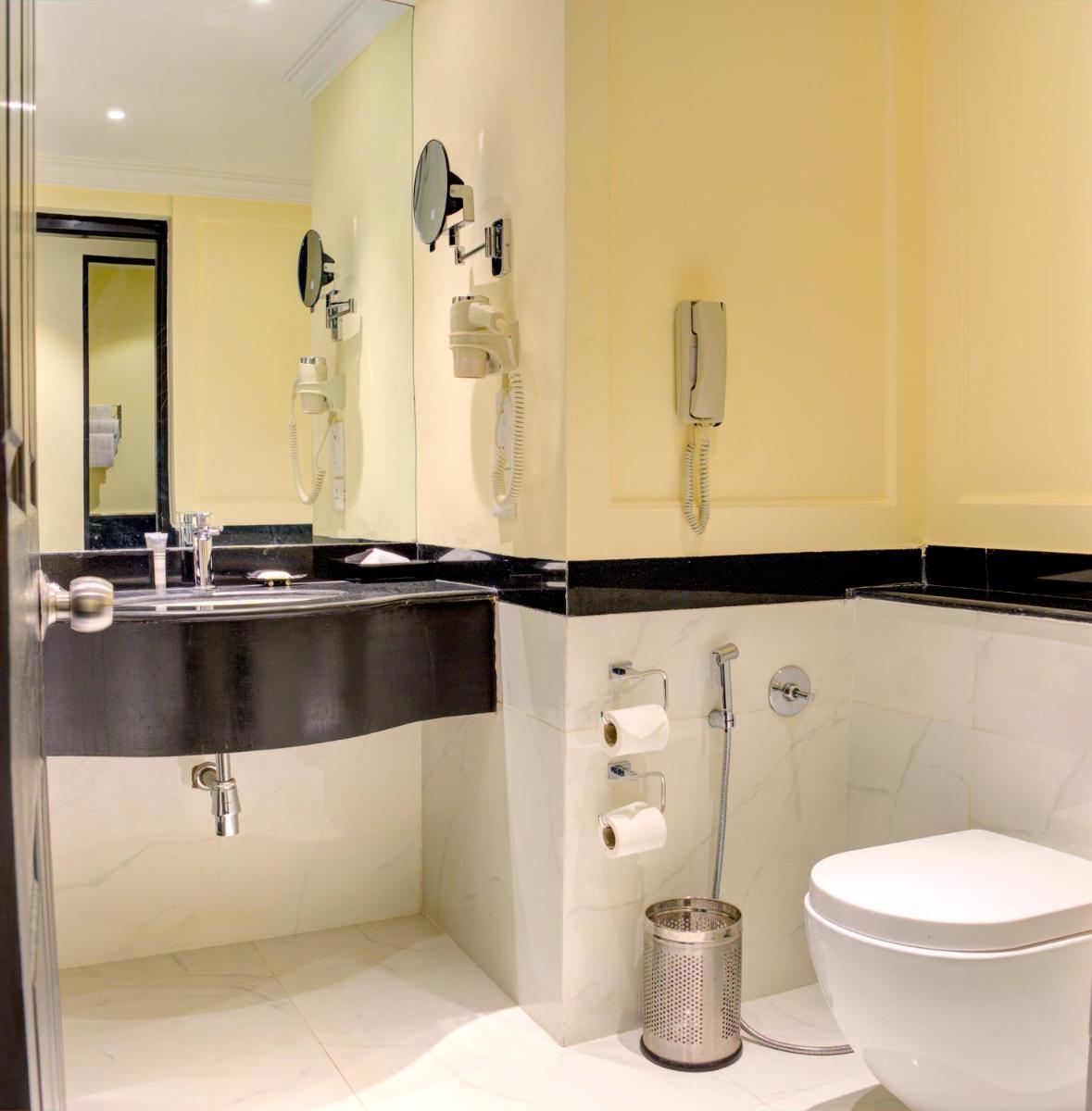 a bathroom with a toilet and a sink and a phone at Hotel Royal Orchid Bangalore in Bengaluru