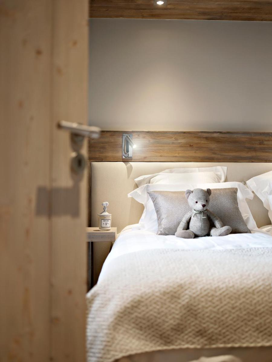 un ours en peluche assis sur un lit dans l'établissement MGM Hôtels & Résidences - Résidence Chalets Laska, aux Contamines-Montjoie