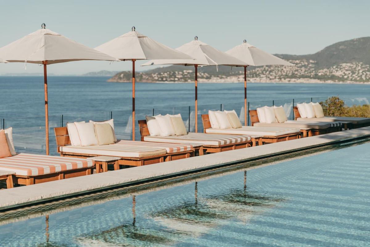 une rangée de chaises longues et de parasols à côté d'une piscine dans l'établissement Lily of the Valley, à La Croix-Valmer