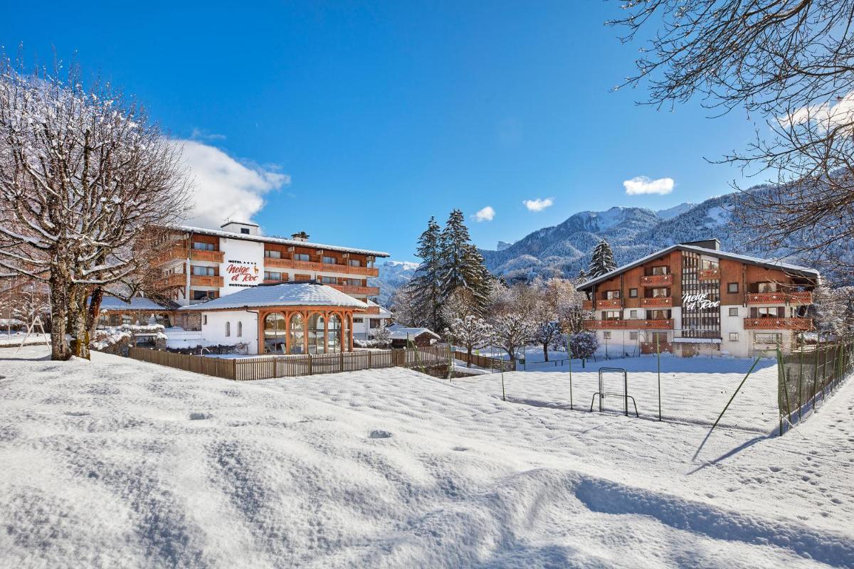 un bâtiment sous la neige avec des montagnes en arrière-plan dans l'établissement Chalet-Hôtel Neige et Roc, The Originals Relais, à Samoëns