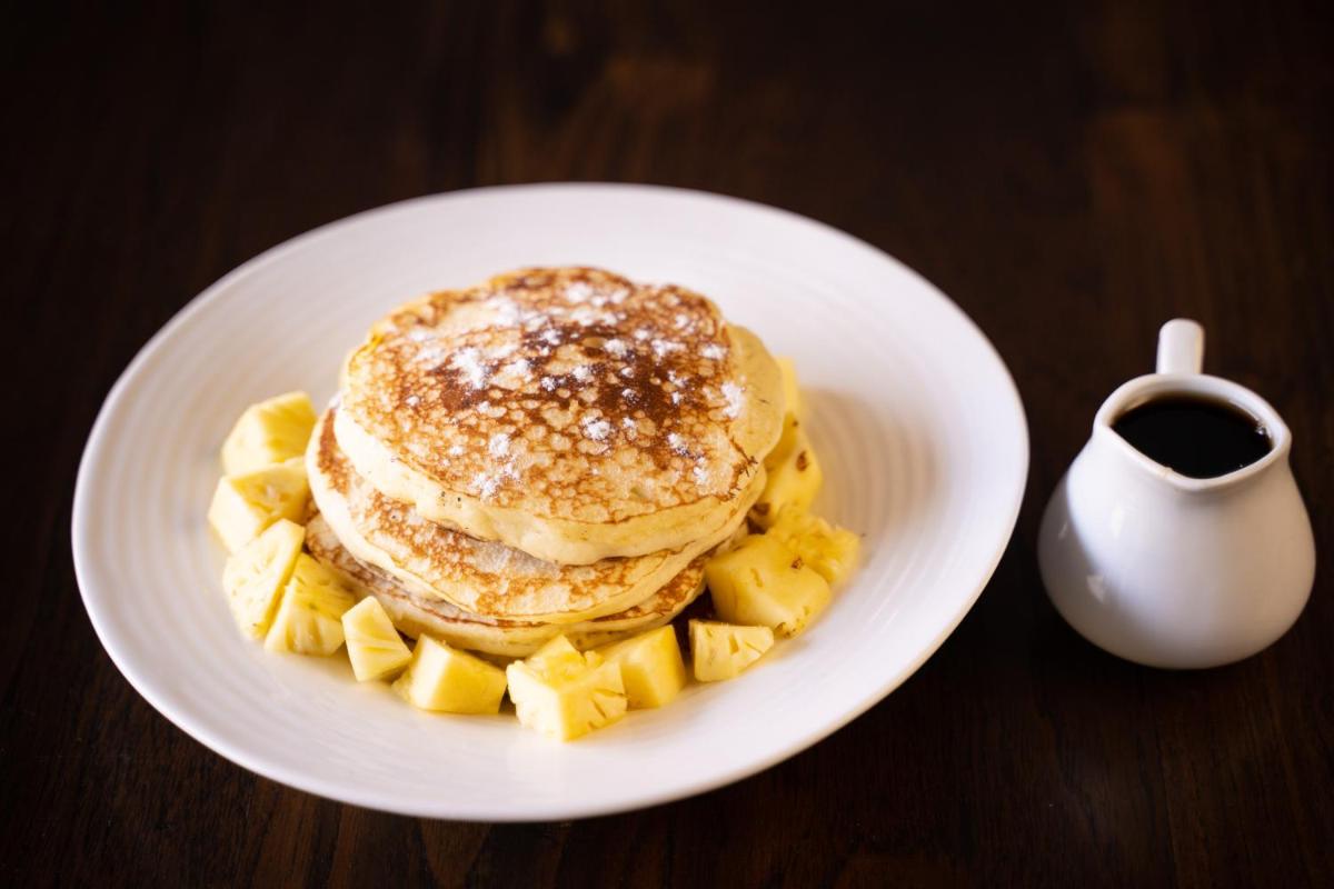 a white plate with a stack of pancakes and pineapple at Antalya By Divine Ganga Cottage in Rishīkesh