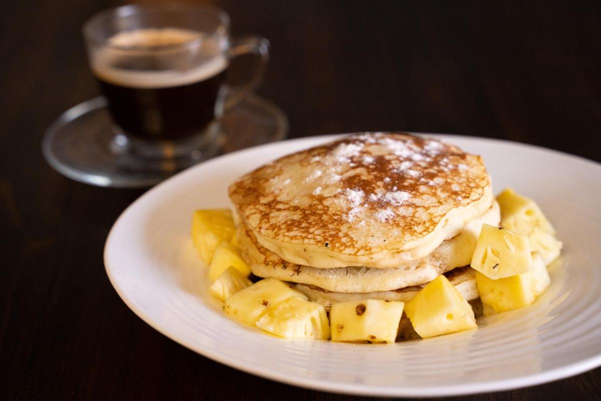a white plate with a stack of pancakes and pineapple at Antalya By Divine Ganga Cottage in Rishīkesh