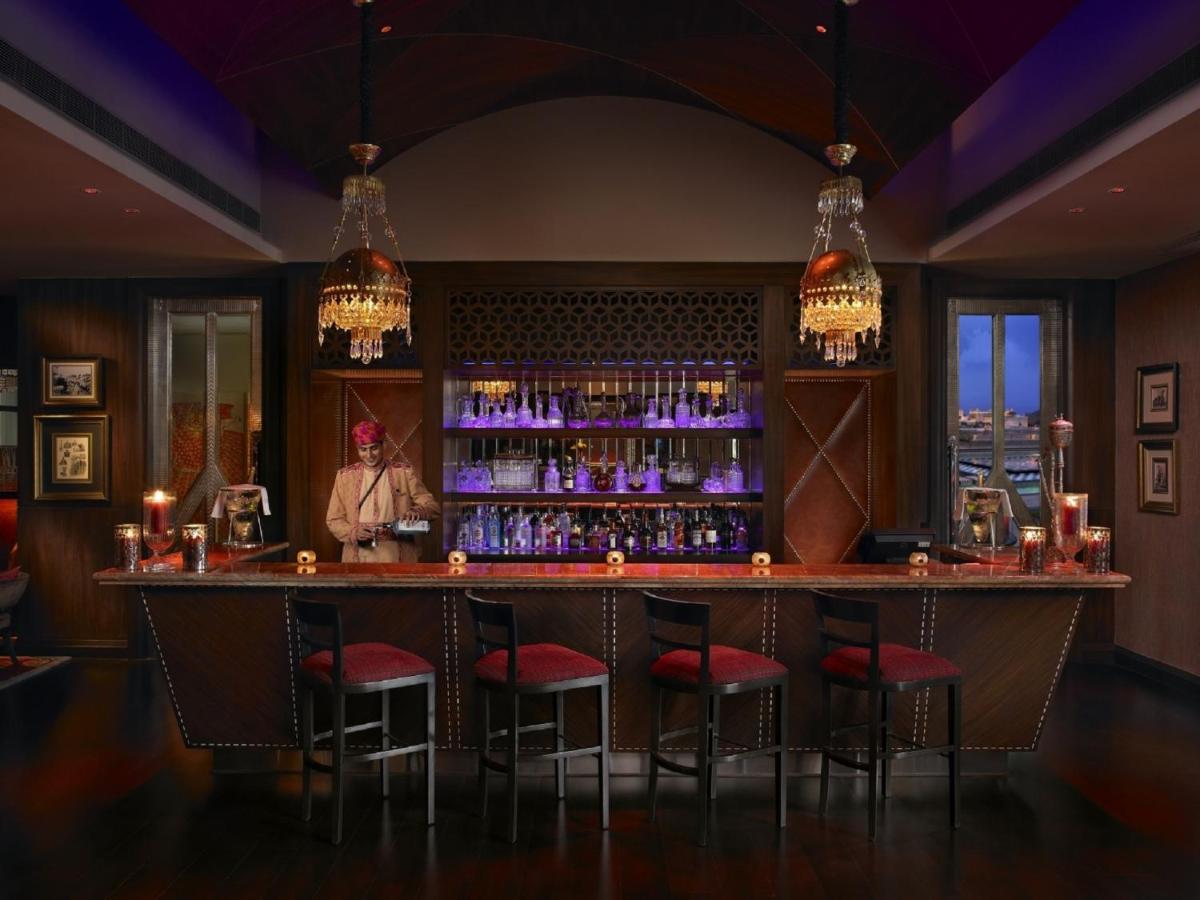 a bar with red chairs and a man standing behind it at The Leela Palace Udaipur in Udaipur
