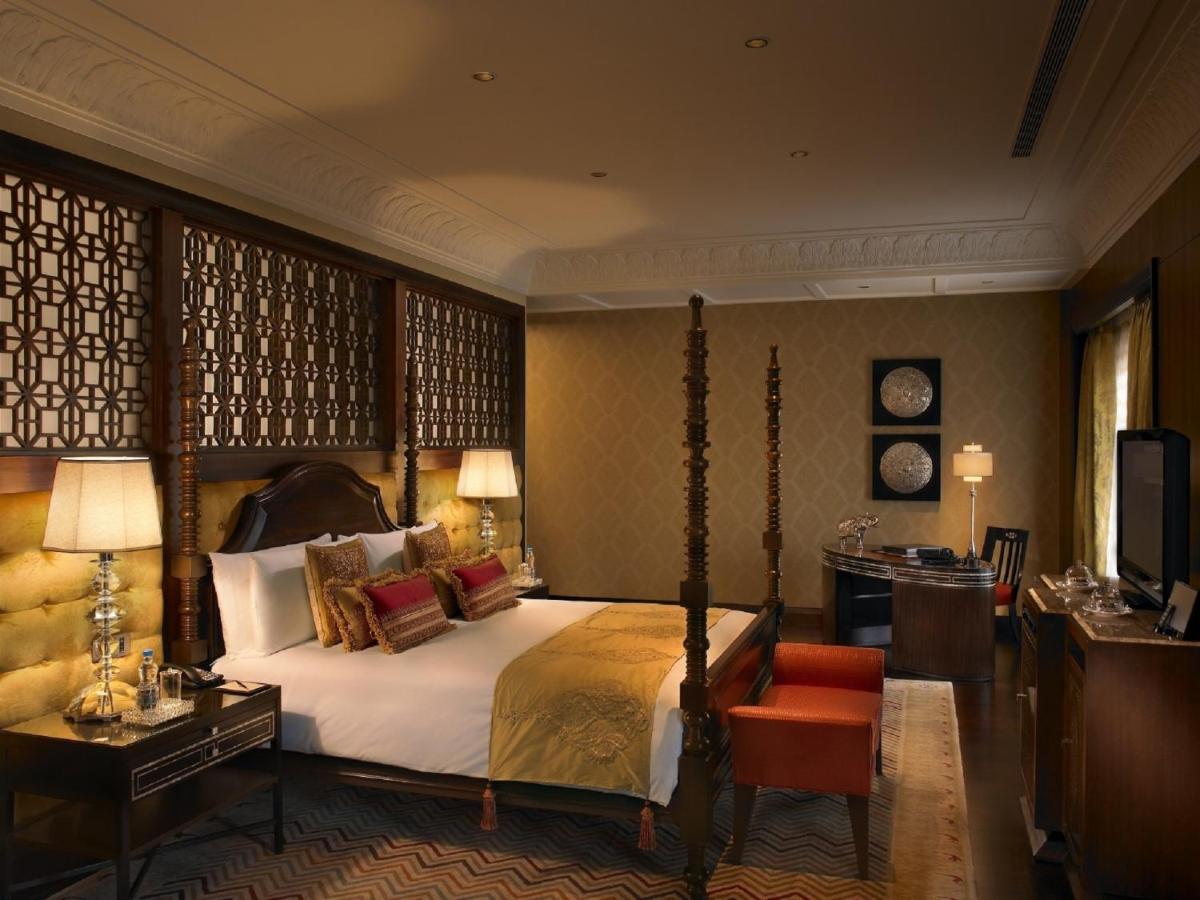 a bedroom with a bed and a desk and a television at The Leela Palace Udaipur in Udaipur