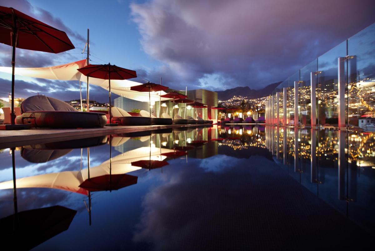 uma piscina com guarda-sóis e uma cidade à noite em The Vine Hotel no Funchal
