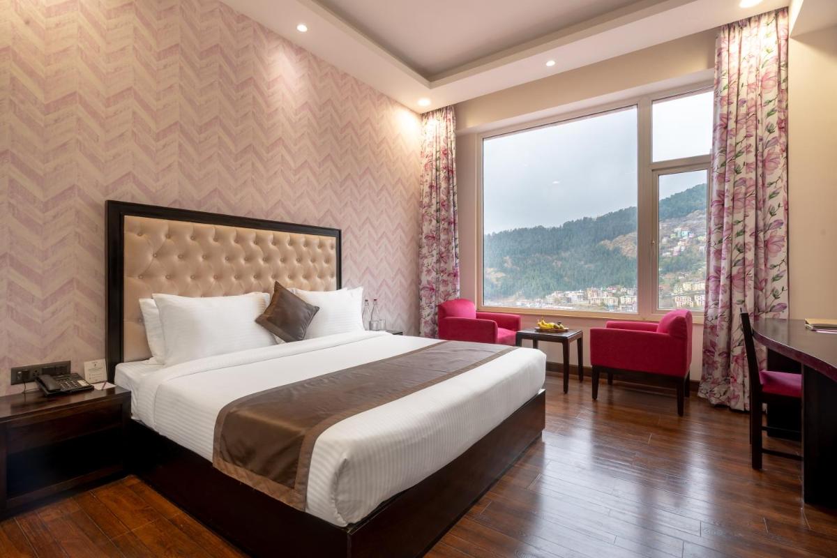 a hotel room with a bed and a desk and a window at The Orchid Shimla in Shimla