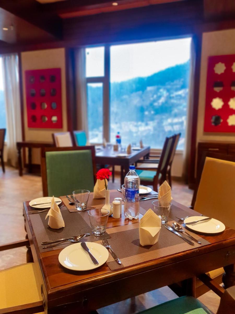 a wooden table with plates and utensils in a restaurant at The Orchid Shimla in Shimla