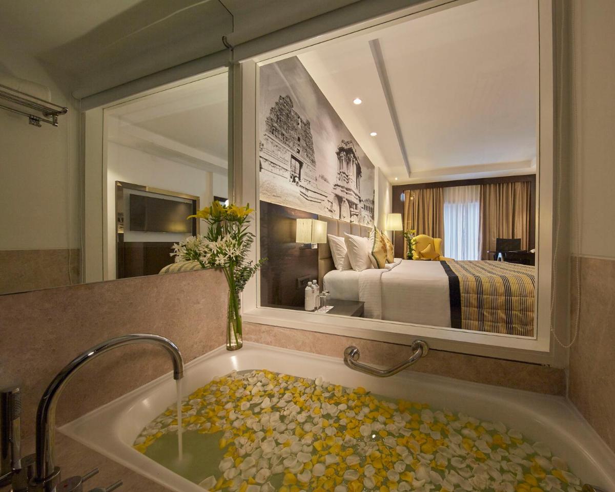 a bathroom with a bath tub with a bedroom at Hotel Royal Orchid Bangalore in Bengaluru