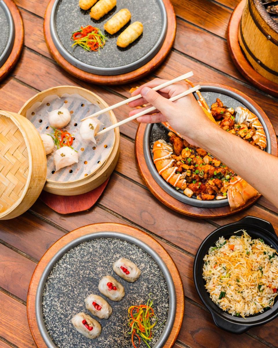 a table with plates of food and a person holding chopsticks at Shangri-La Eros New Delhi in New Delhi a table with plates of food and a person holding chopsticks at Shangri-La Eros New Delhi in New Delhi