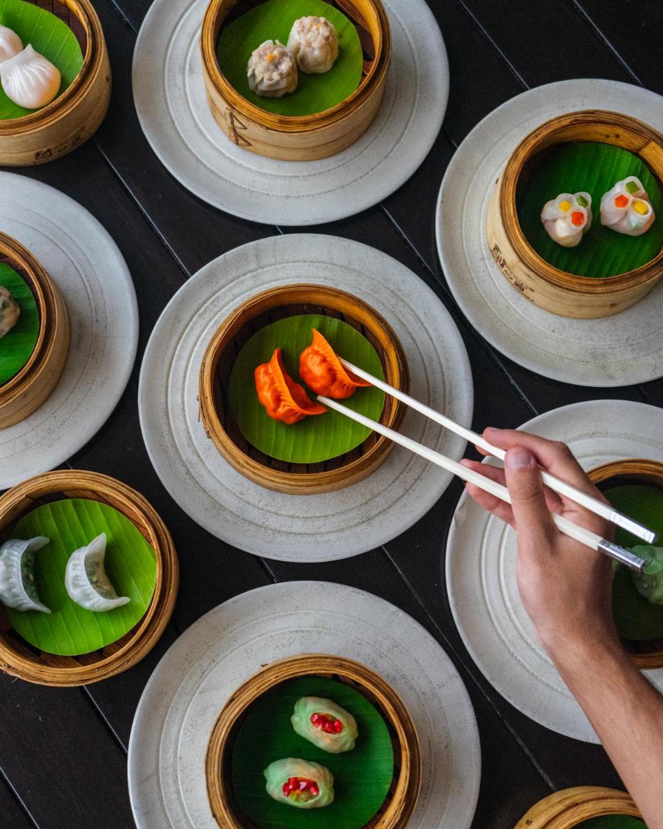 a person holding chopsticks over plates of food on a table at Shangri-La Bengaluru in Bengaluru a person holding chopsticks over plates of food on a table at Shangri-La Bengaluru in Bengaluru