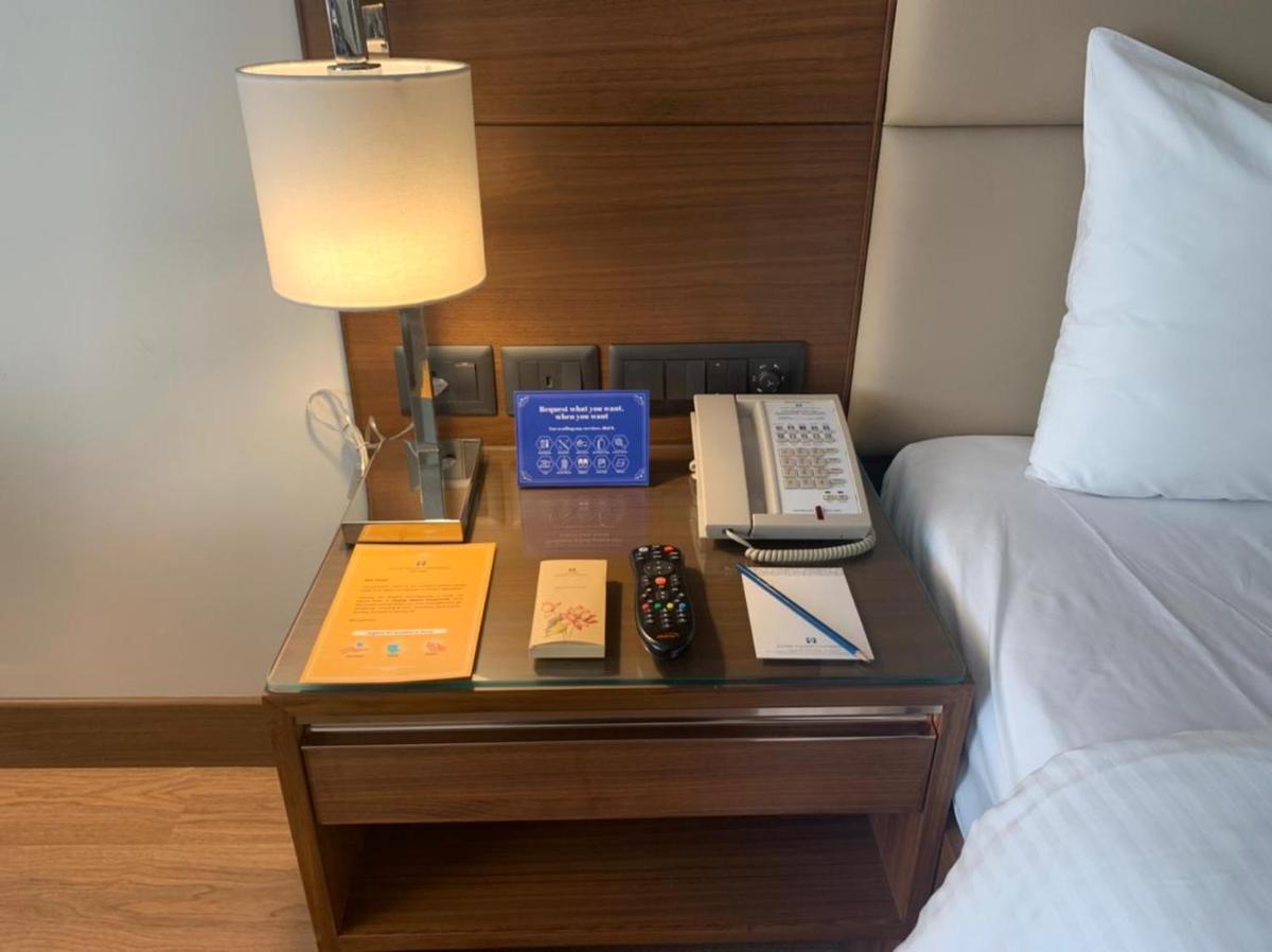 a nightstand with a bed and a lamp and a phone at Jaypee Vasant Continental in New Delhi