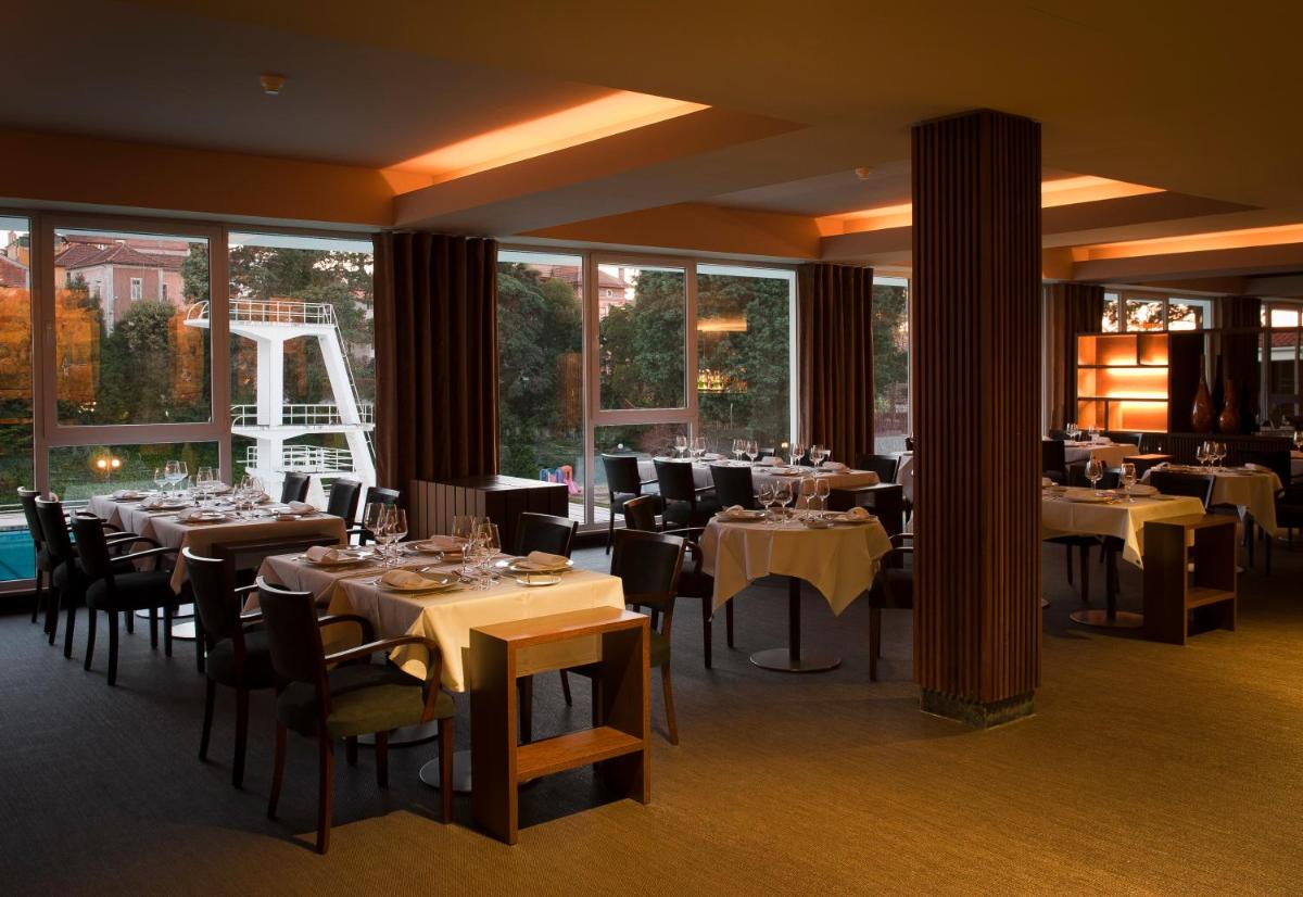 uma sala de jantar com mesas, cadeiras e janelas em Grande Hotel De Luso no Luso