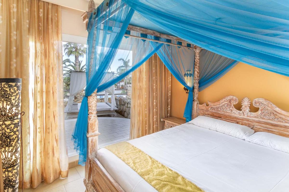 1 dormitorio con cama con dosel y cortinas azules en El Cortijo de Zahara by QHotels, en Zahara de los Atunes