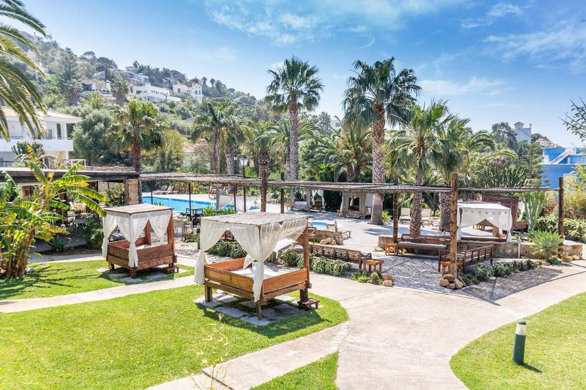 un resort con piscina y palmeras en El Cortijo de Zahara by QHotels, en Zahara de los Atunes