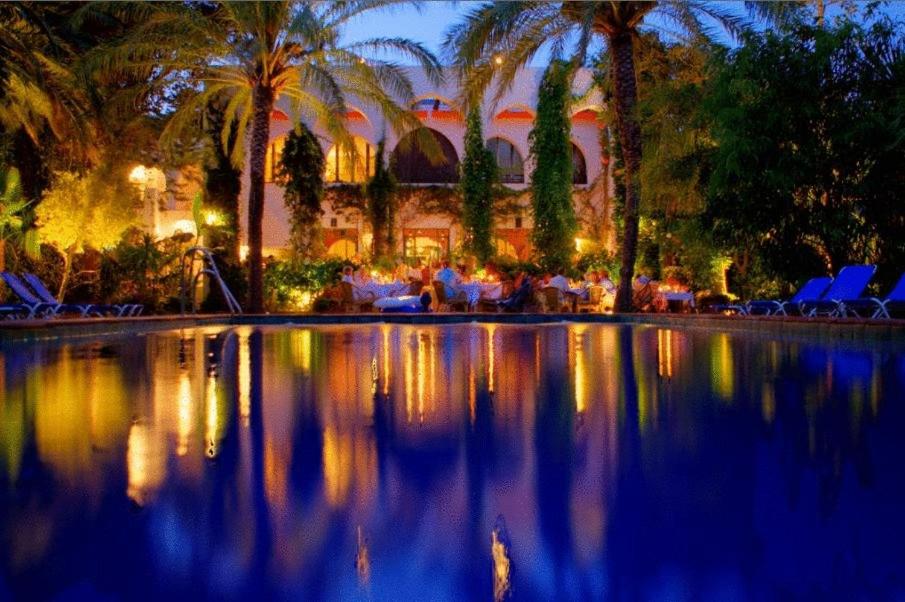 un grupo de personas sentadas alrededor de una piscina por la noche en Hurricane Beach Hotel, en Tarifa