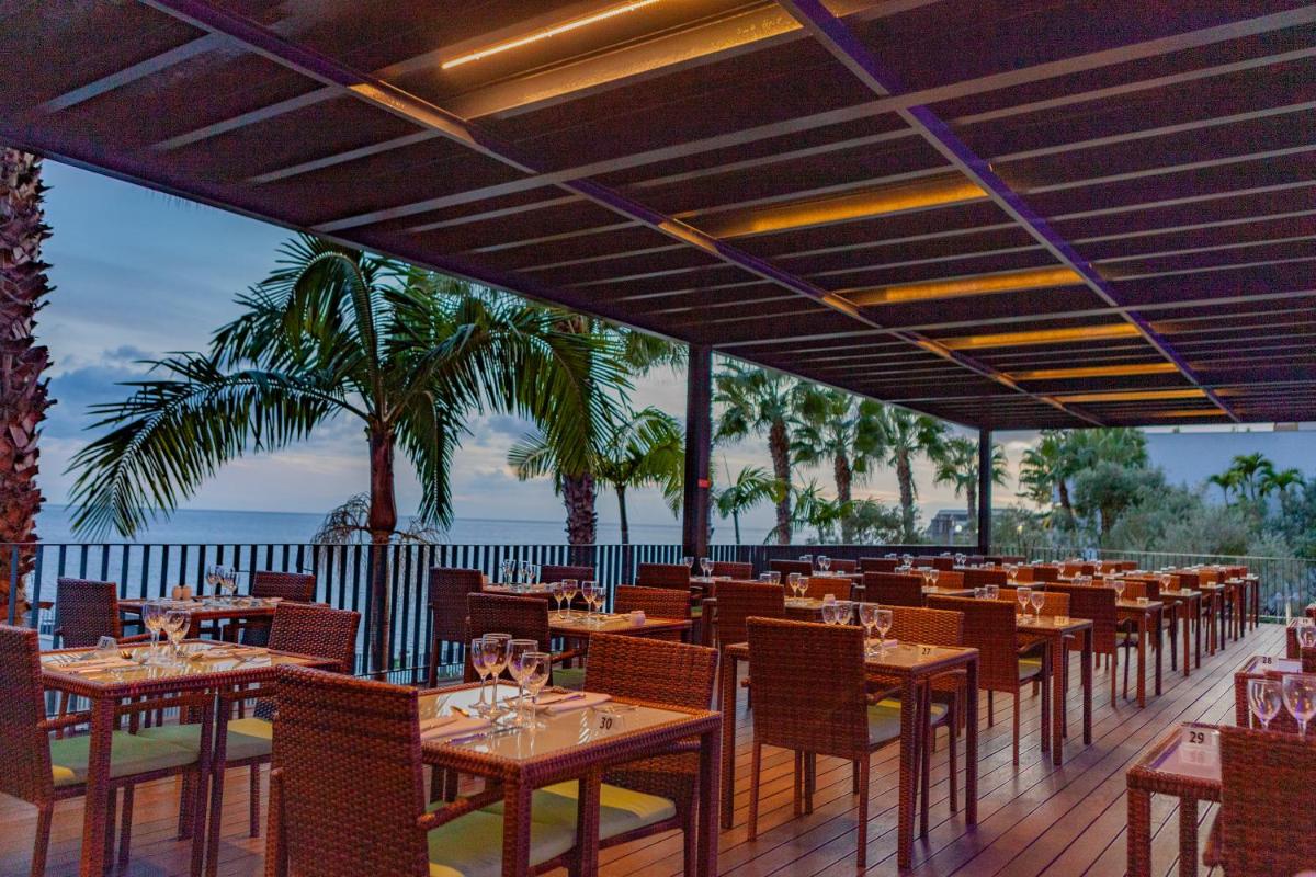 um restaurante com mesas e cadeiras com o oceano ao fundo em VidaMar Resort Hotel Madeira no Funchal