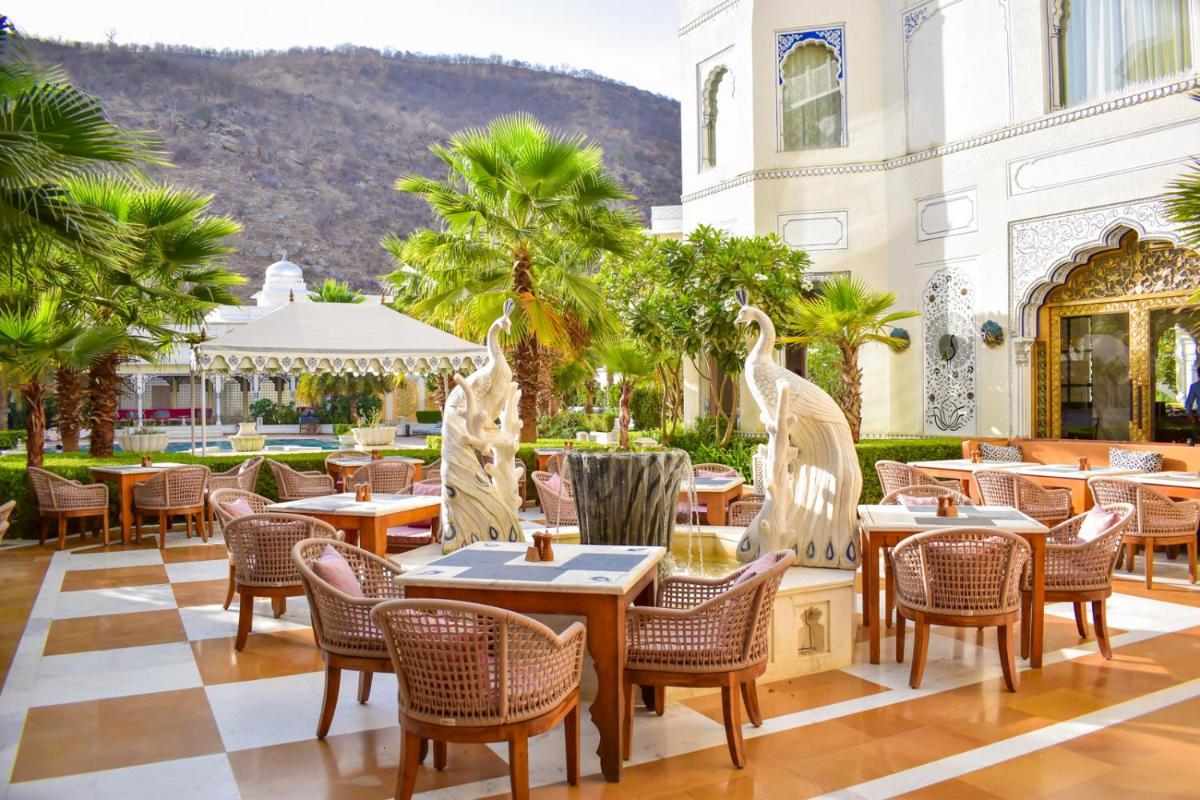 a restaurant with tables and chairs and palm trees at The Leela Palace Jaipur in Jaipur
