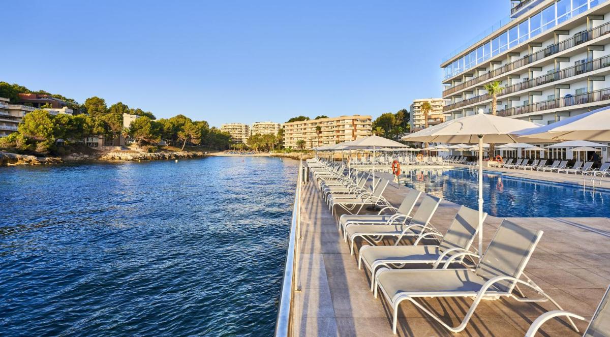Una fila de tumbonas junto a un cuerpo de agua. en Globales Cala Viñas Adults Only 16+, en Cala Vinyes