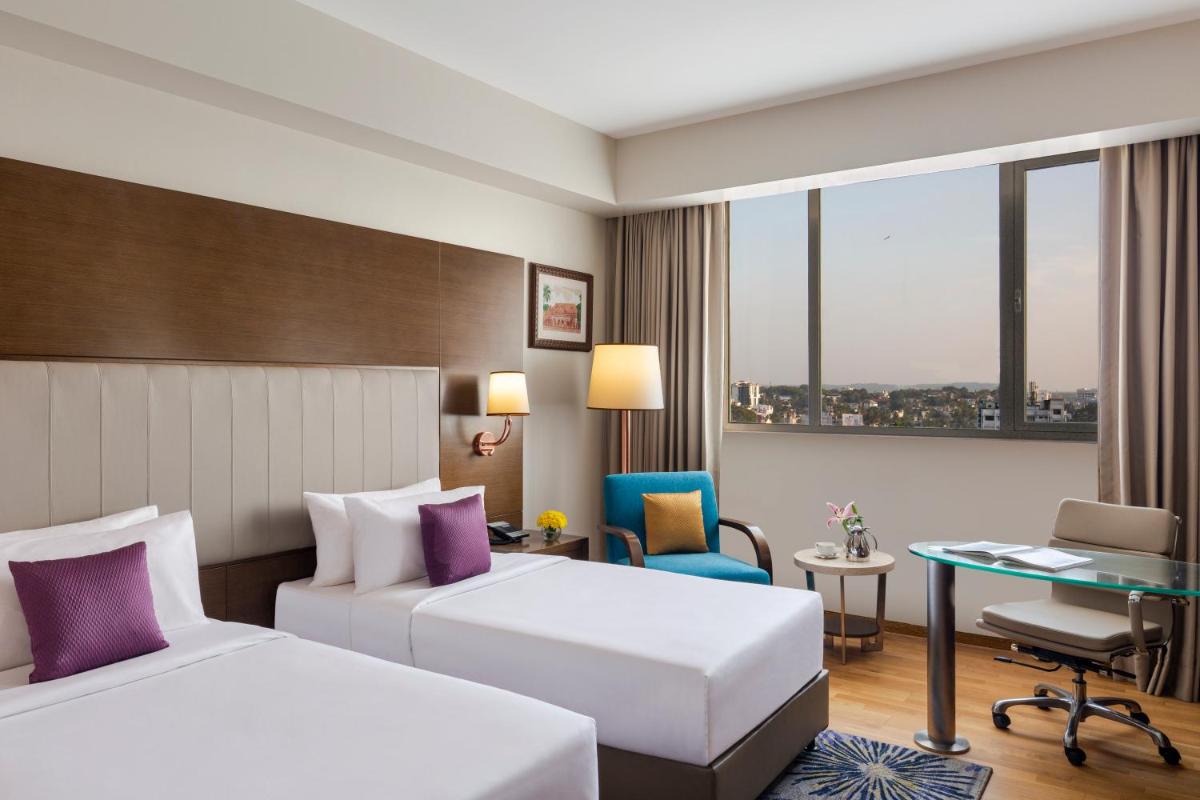 a hotel room with two beds and a desk at Vivanta Thiruvananthapuram in Trivandrum