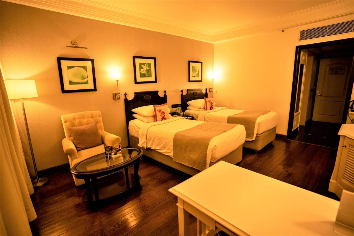 a hotel room with two beds and a chair at Hotel Royal Orchid Bangalore in Bengaluru