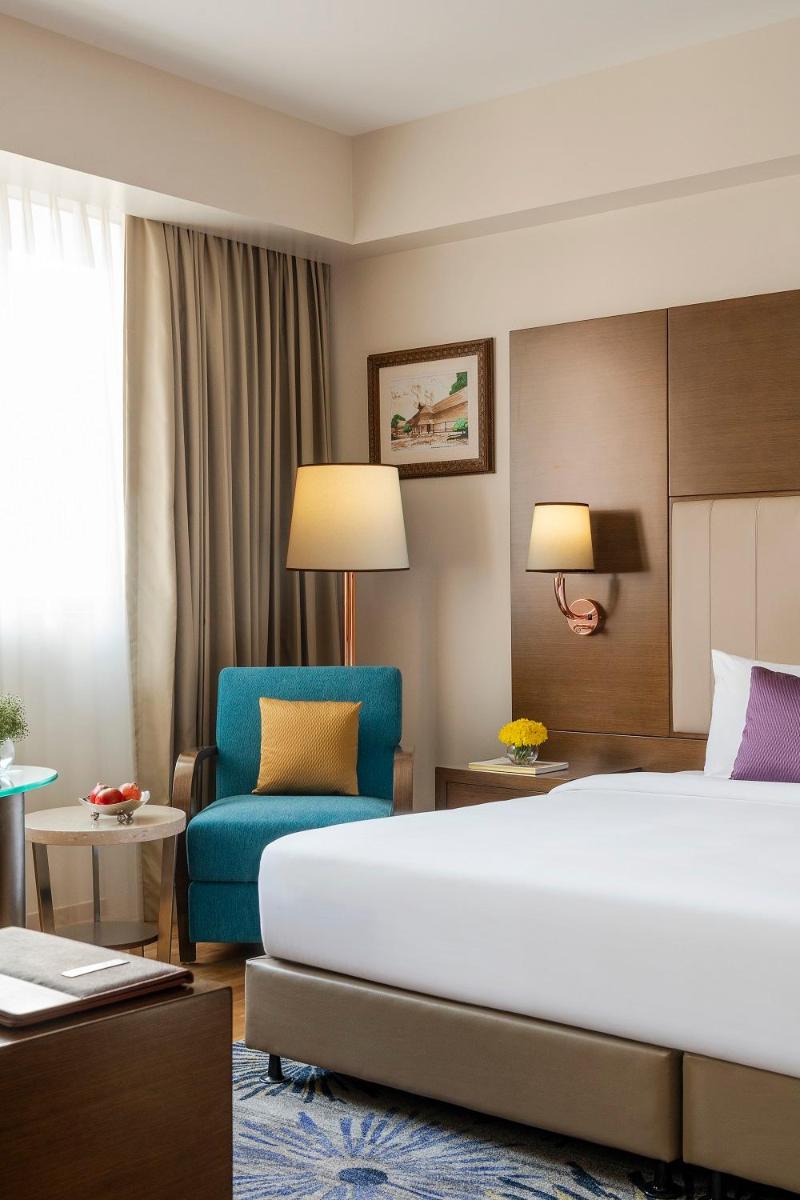 a hotel room with a bed and a blue chair at Vivanta Thiruvananthapuram in Trivandrum