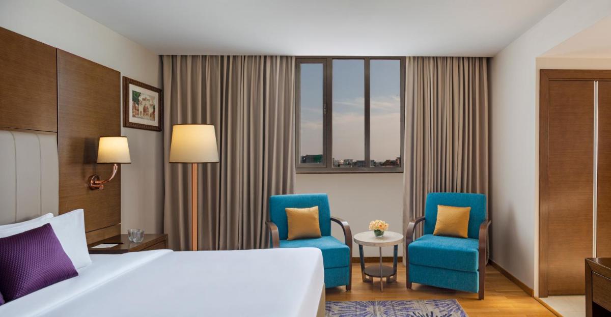 a hotel room with a bed and two blue chairs at Vivanta Thiruvananthapuram in Trivandrum