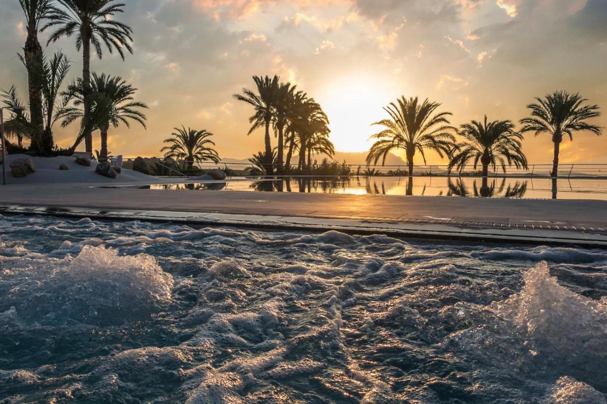 Una piscina con palmeras y el océano al atardecer. en Balneario de Leana, en Fortuna