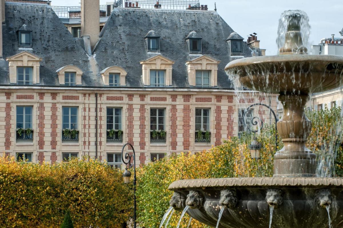 une fontaine devant un grand bâtiment dans l'établissement Cour des Vosges - Evok Collection, à Paris une fontaine devant un grand bâtiment dans l'établissement Cour des Vosges - Evok Collection, à Paris
