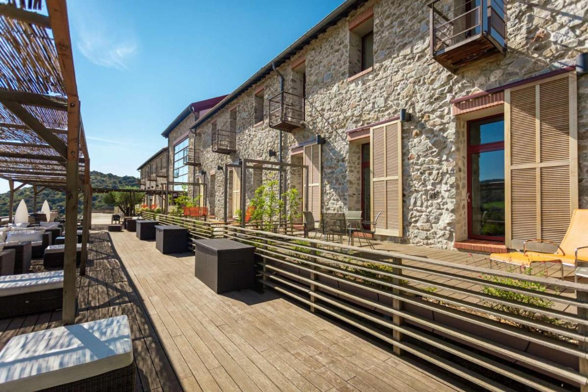un bâtiment en pierre avec une terrasse aménagée avec des tables et des chaises dans l'établissement Domaine Riberach - Hotel 4 - Restaurant gastronomique - Spa - Piscine - Vignoble, à Bélesta