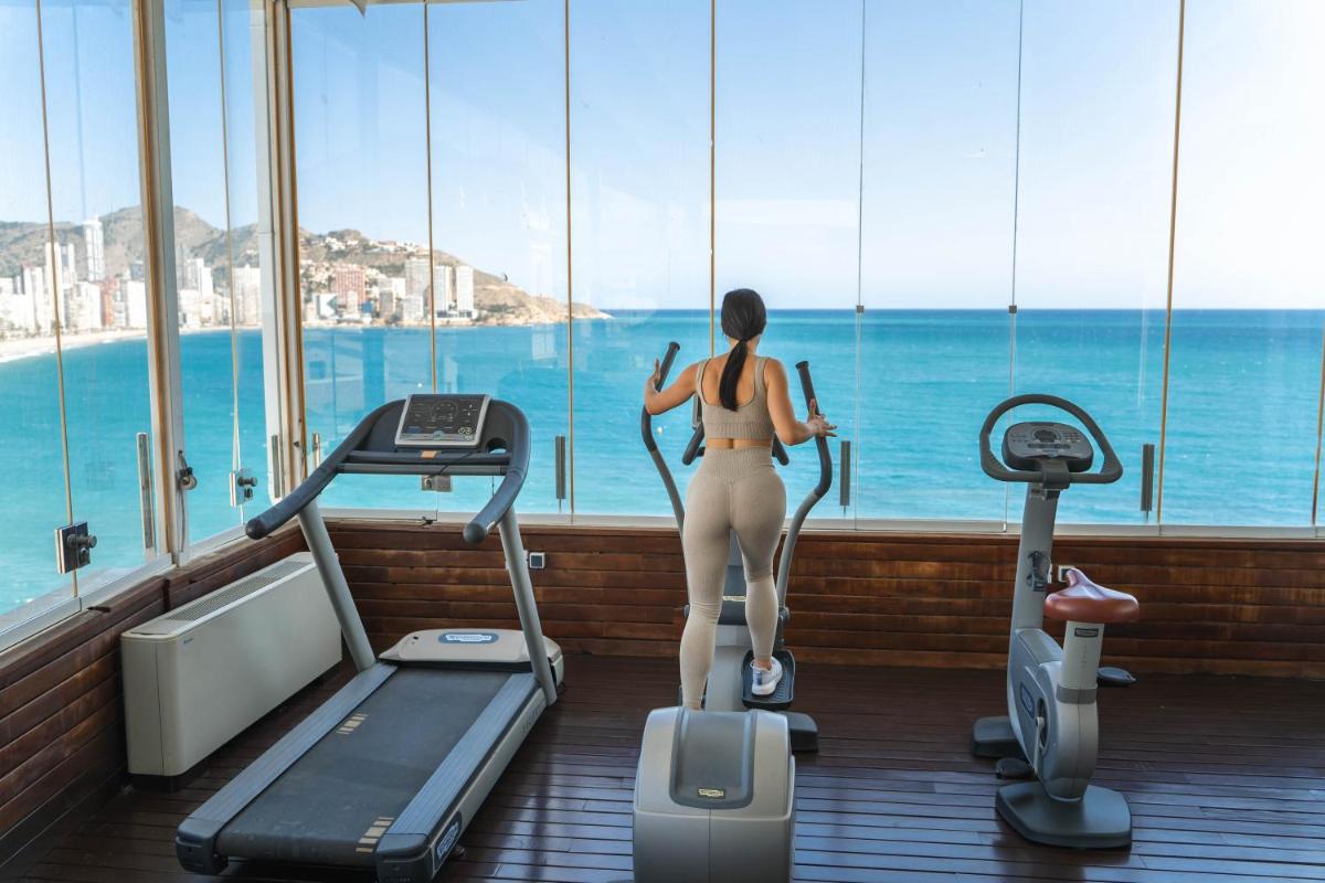 Una mujer en una cinta de correr en un gimnasio mirando el océano. en Hotel Boutique Villa Venecia, en Benidorm