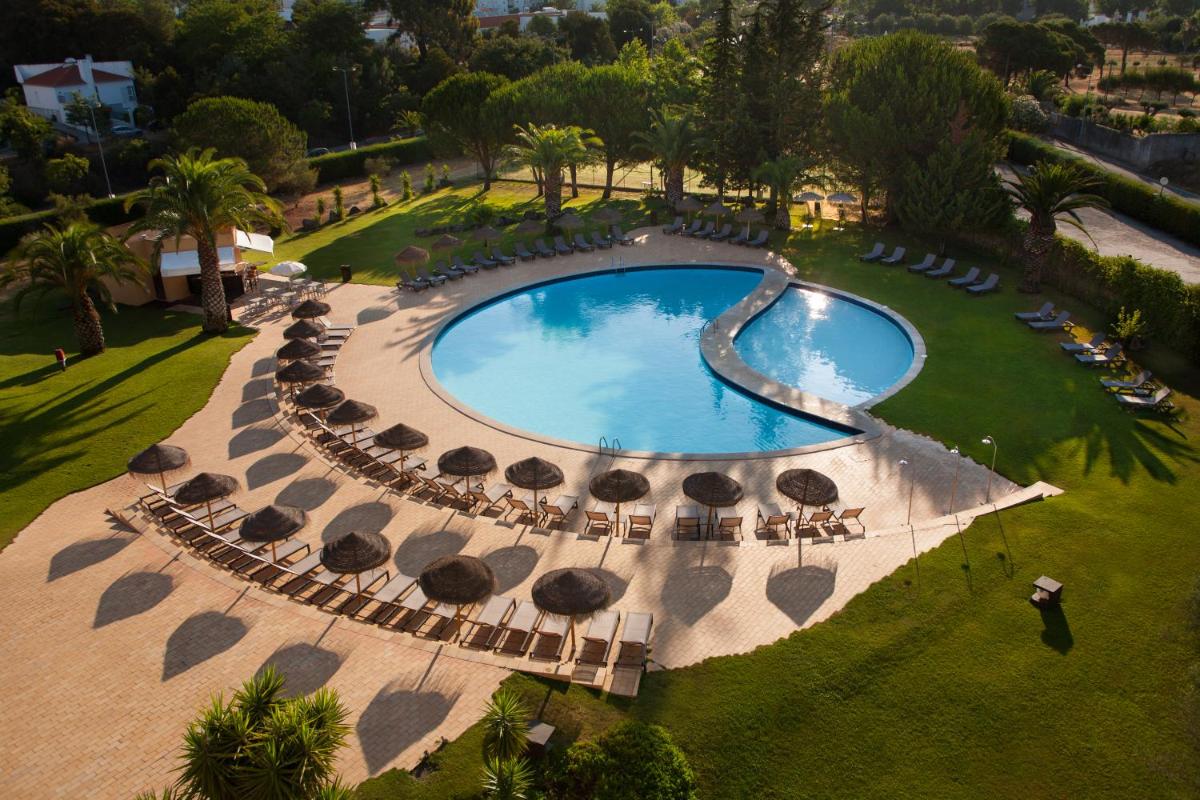 Vista aérea de uma piscina com guarda-sóis e cadeiras. em Evora Hotel em Évora