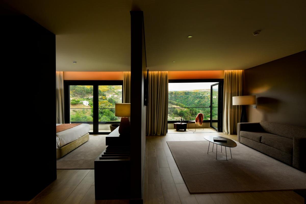 um quarto com uma cama e uma sala de estar com uma grande janela em MW Douro Wine & Spa em Santa Marta de Penaguião