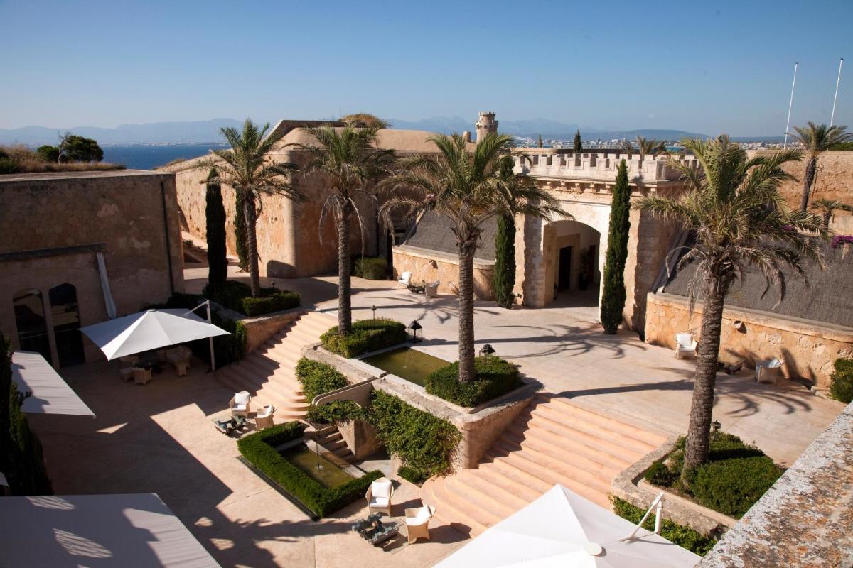 un patio con palmeras, mesas y sombrillas en Cap Rocat, a Small Luxury Hotel of the World, en Cala Blava