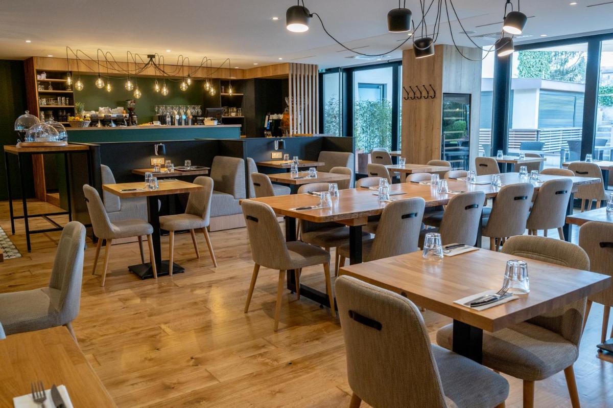 un restaurant avec des tables et des chaises en bois ainsi qu'un bar dans l'établissement Domaine la Charpinière, The Originals Collection, à Saint-Galmier