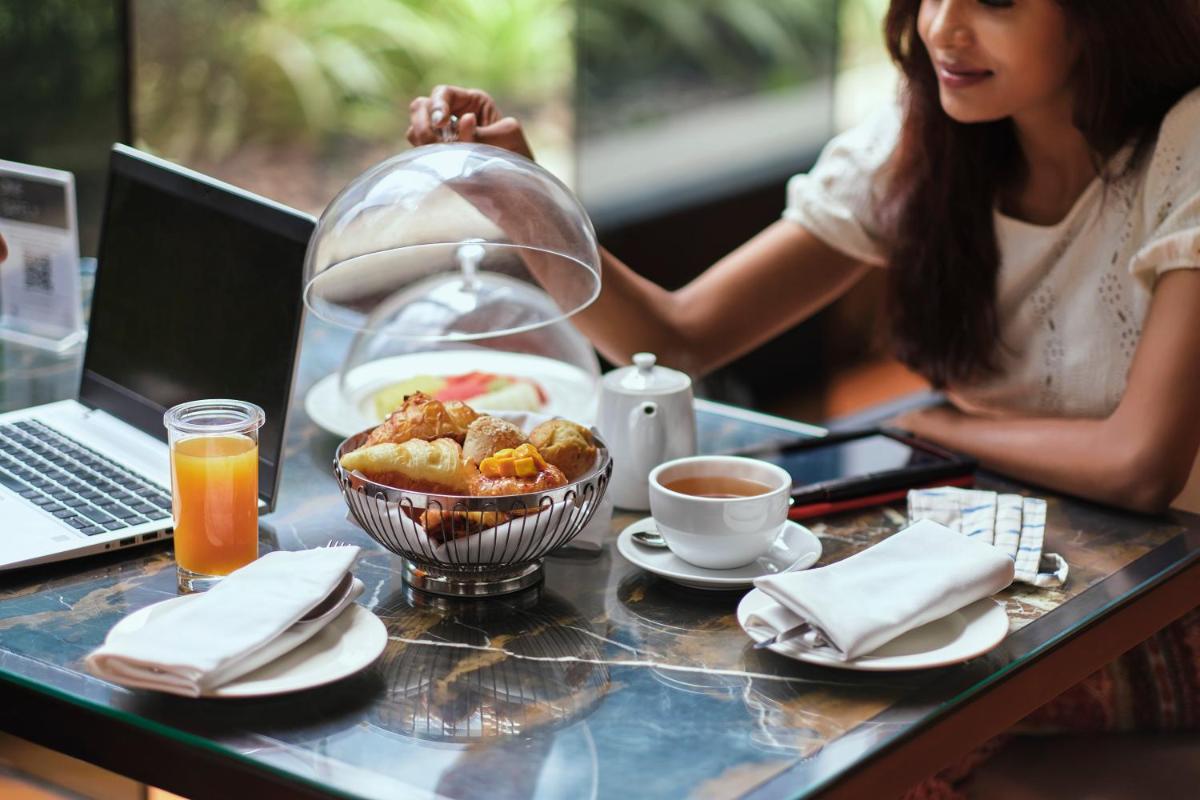a woman sitting at a table with a bowl of food and a laptop at Hyatt Regency Gurgaon in Gurgaon