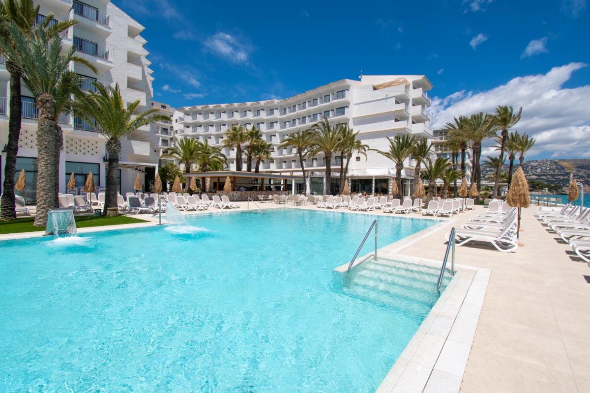 Una gran piscina con sillas y un hotel. en Hotel Cap Negret, en Altea